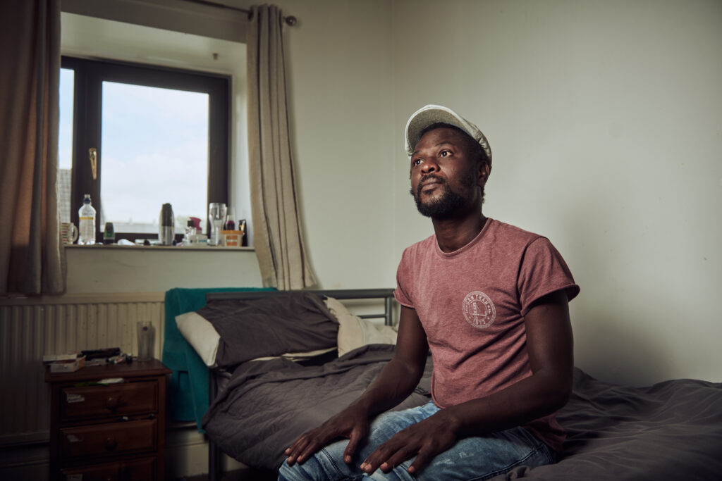 The Wallich male service user in their temporary accommodation, sitting on their bed - Wales 