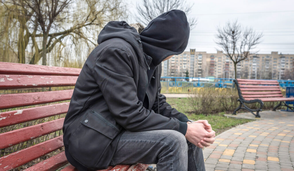 A man in a hood sitting on a bench.