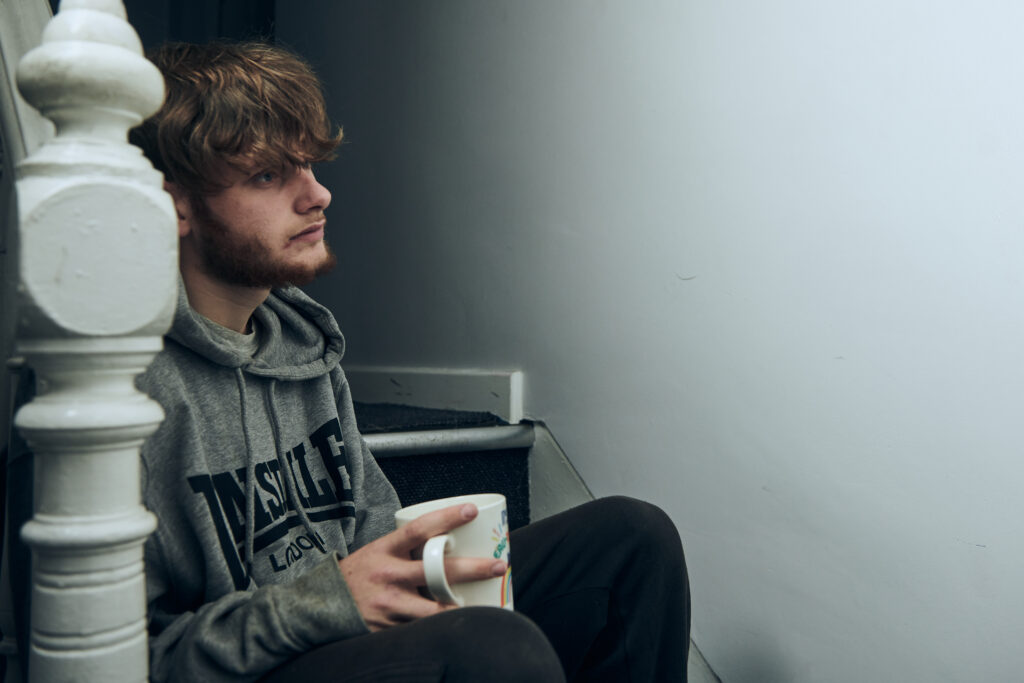 Young person sitting on stairs and holding a mug, Families Temporary Accommodation Project