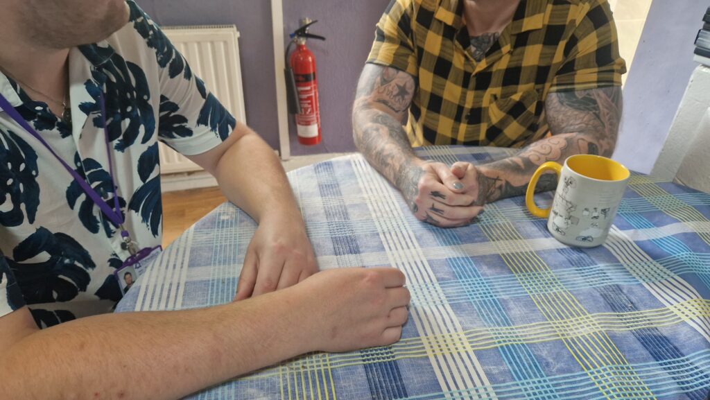 Two people sitting at a table. Both are wearing colourful short-sleeve shirts. We cannot see their faces.