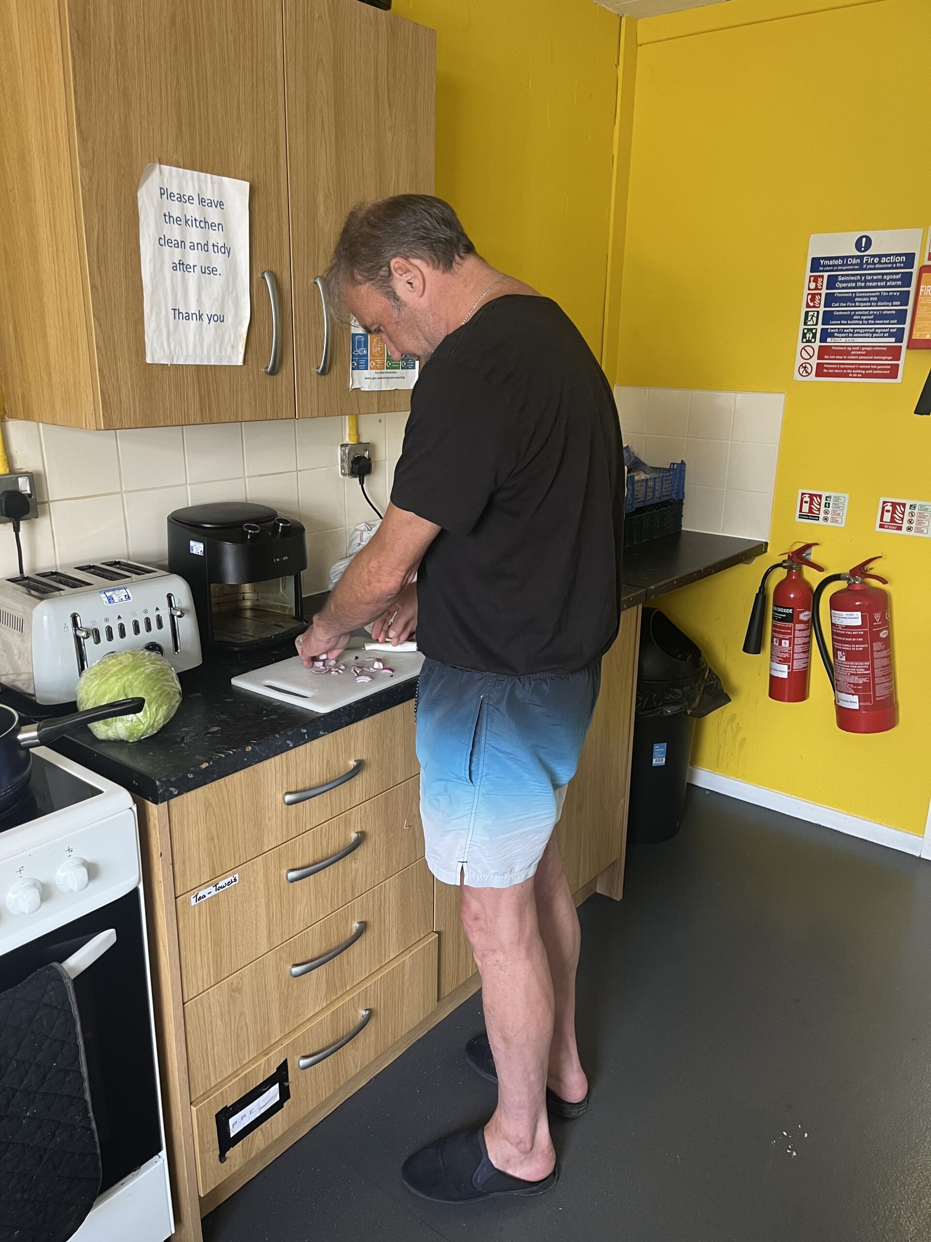 A man preparing food in a kitchen with bright yellow walls.
