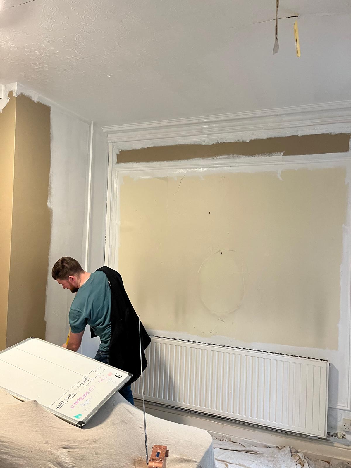 Man painting a wall, surrounded by dust covers