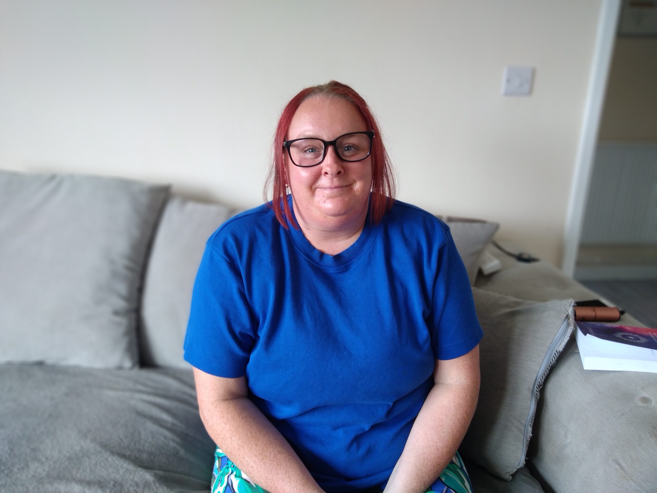 A woman with red hair, wearing a blue t-shirt. She is smiling and looks confident.