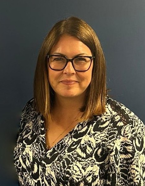 A woman with brown shoulder-length hair and black glasses, wearing a black and white patterned dress